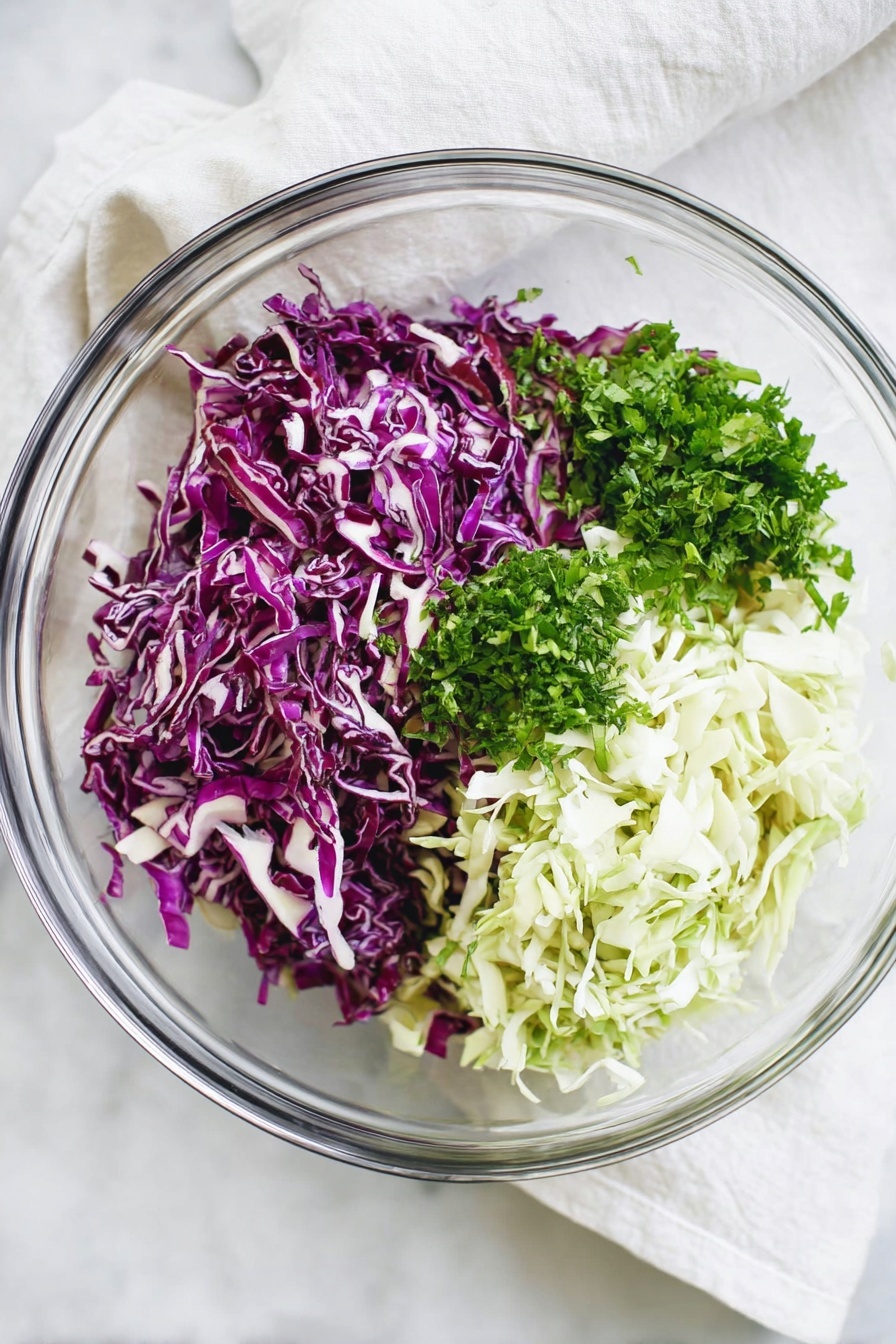 The image shows a clear glass bowl on a white marbled surface filled with three main layers of shredded vegetables. On the left side is a pile of bright purple cabbage with thin white veins. On the right side is a mix of white and light green cabbage, finely shredded. Above the cabbages, near the top center of the bowl, is a small pile of bright green chopped herbs, likely parsley or cilantro, adding a fresh contrast. The bowl is set next to a soft white cloth. Photo taken with an iphone --ar 2:3 --v 7